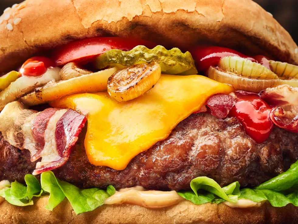 Detailaufnahme eines saftigen Burgers mit geschmolzenen Käse, Bacon und Zwiebeln.