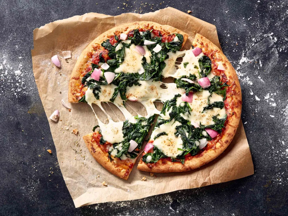 Detailfoto angeschnittener Pizza mit Spinat, Zwiebeln und verlaufendem Mozzarella
